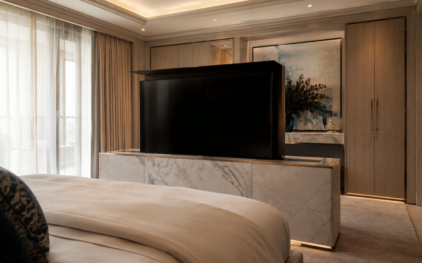 Hidden TV lift rising from a marble console at the foot of a luxury master bed