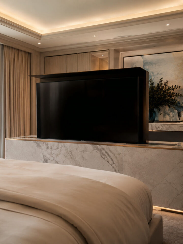 Hidden TV lift rising from a marble console at the foot of a luxury master bed